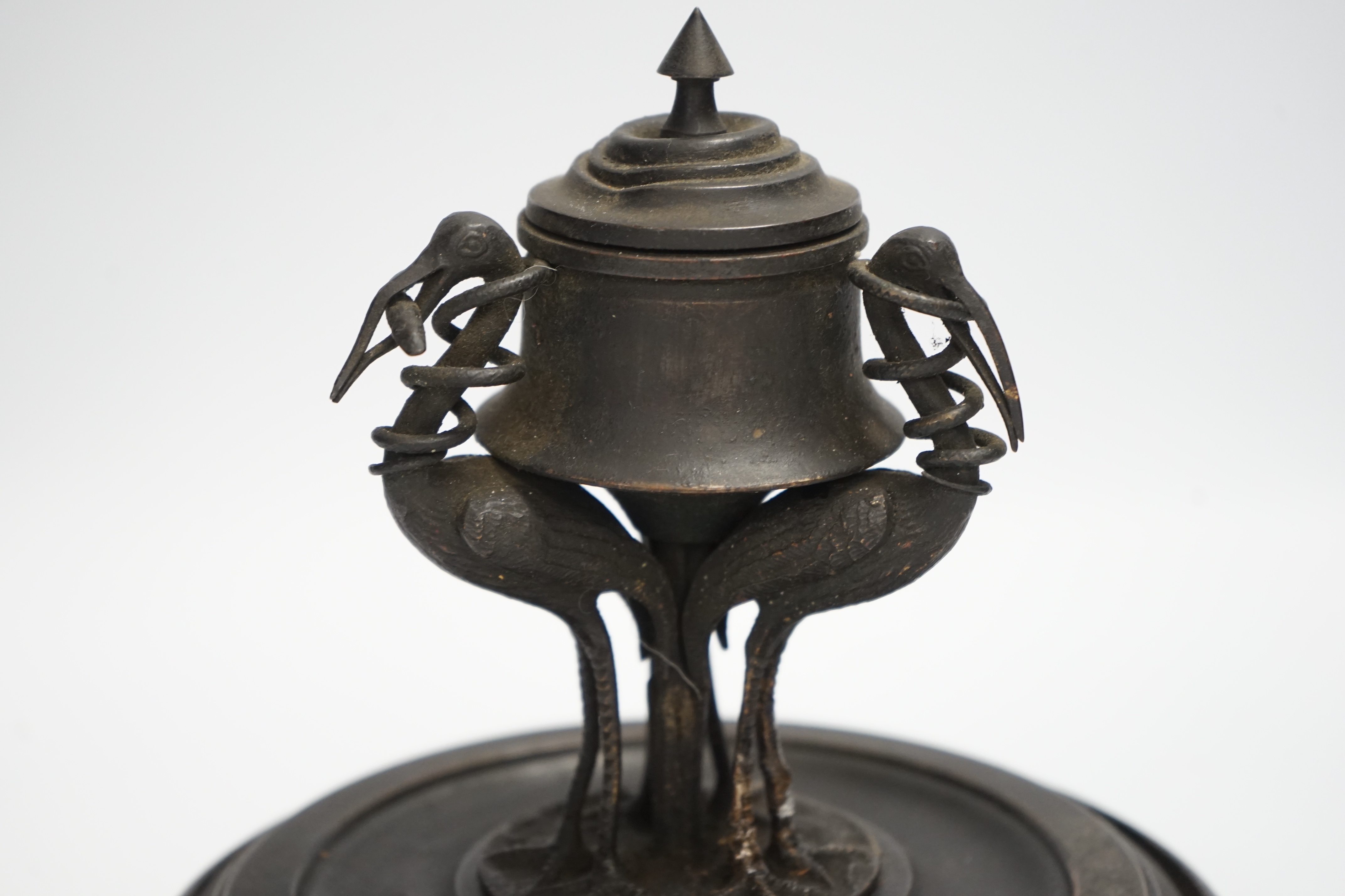 A late 19th century patinated metal inkwell, modelled with three cranes on an ebonised pine base, 18cm